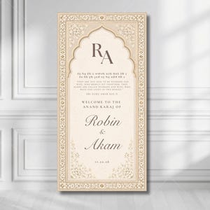 Op de afbeelding: Een rechthoekig welkomstbord voor een bruiloft in crème en beige met een sierlijke bloemenrand. Het bevat de initialen RA, de tekst Welcome to the Anand Karaj of Robin & Akam, een citaat en de datum 11.22.26 in donkerbruine schreefletters.