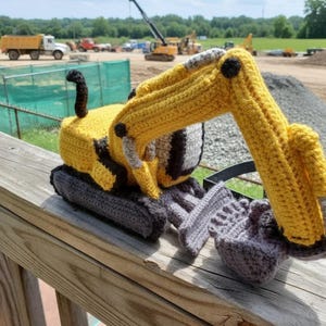 May include: A handmade crochet excavator toy in yellow, gray, and black. The toy features a detailed design with a movable arm and bucket, perfect for imaginative play. The excavator is approximately 10 inches long.