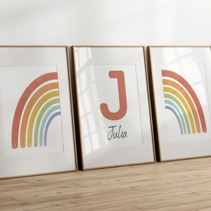 Puede incluir: Tres impresiones enmarcadas con un diseño de arcoíris. La impresión del medio presenta una gran letra J roja y el nombre Julia.