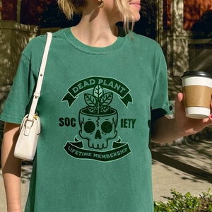 May include: A green t-shirt with a skull and crossbones graphic. The graphic says "Dead Plant Society" and "Lifetime Membership".