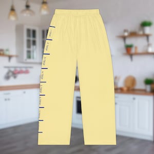 A pair of light yellow pajama pants with a graphic print down the leg that resembles the hatch marks on a stick of butter. the front left of the pants also has a graphic that reads "SALTED BUTTER net wt 4 oz"