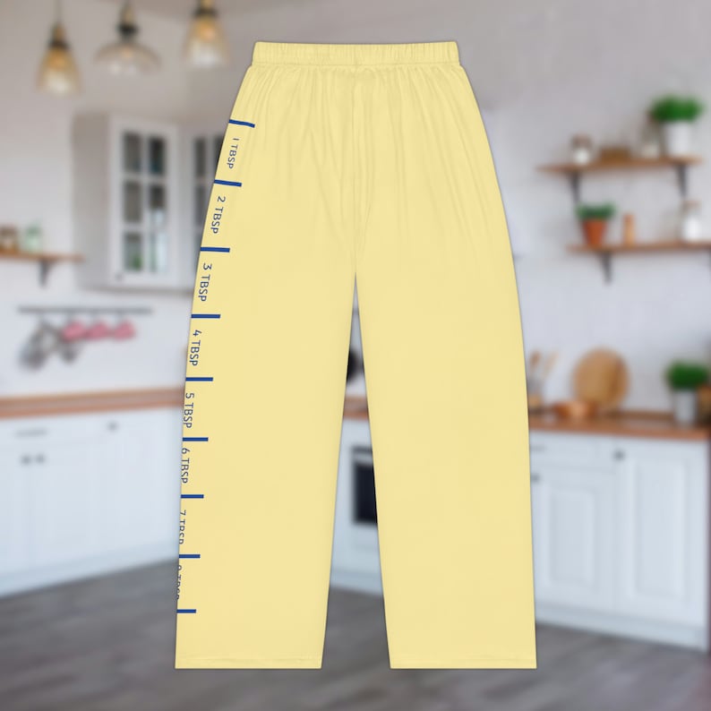 A pair of light yellow pajama pants with a graphic print down the leg that resembles the hatch marks on a stick of butter. the front left of the pants also has a graphic that reads "SALTED BUTTER net wt 4 oz"