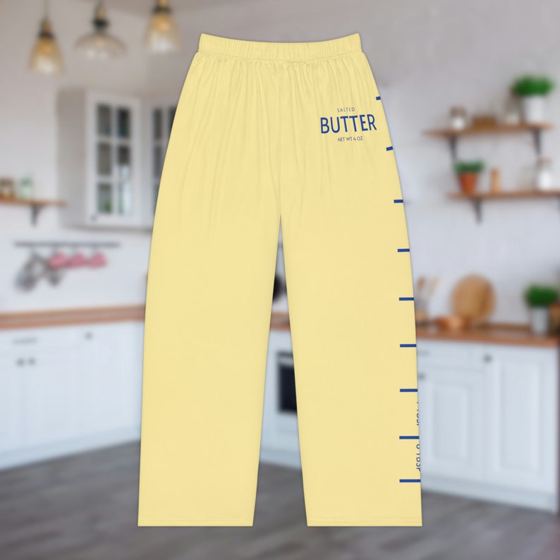 A pair of light yellow pajama pants with a graphic print down the leg that resembles the hatch marks on a stick of butter. the front left of the pants also has a graphic that reads "SALTED BUTTER net wt 4 oz"