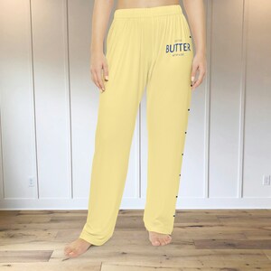 A pair of light yellow pajama pants with a graphic print down the leg that resembles the hatch marks on a stick of butter. the front left of the pants also has a graphic that reads "SALTED BUTTER net wt 4 oz"