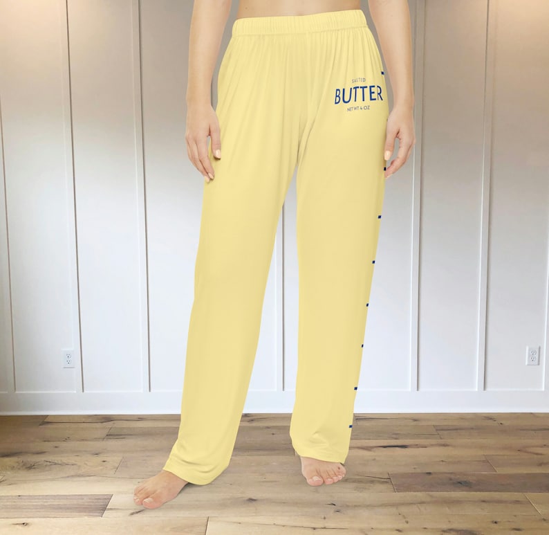 A pair of light yellow pajama pants with a graphic print down the leg that resembles the hatch marks on a stick of butter. the front left of the pants also has a graphic that reads "SALTED BUTTER net wt 4 oz"