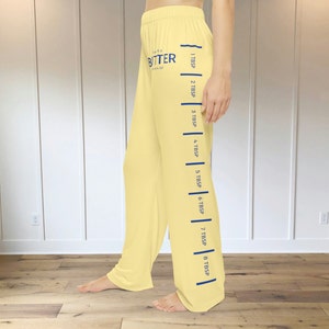 A pair of light yellow pajama pants with a graphic print down the leg that resembles the hatch marks on a stick of butter. the front left of the pants also has a graphic that reads "SALTED BUTTER net wt 4 oz"