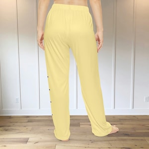 A pair of light yellow pajama pants with a graphic print down the leg that resembles the hatch marks on a stick of butter. the front left of the pants also has a graphic that reads "SALTED BUTTER net wt 4 oz"