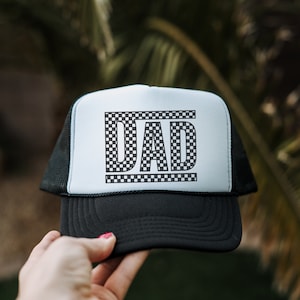 May include: A black and white trucker hat with a white mesh back. The front of the hat has a black and white chequered design that spells out "DAD".