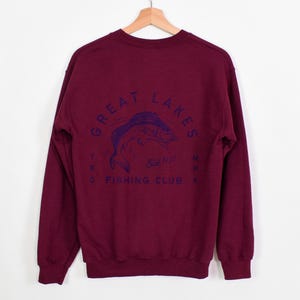 May include: Burgundy long-sleeve sweatshirt with a navy blue graphic of a fish and the text "Great Lakes Trading Co. Fishing Club" on the back.
