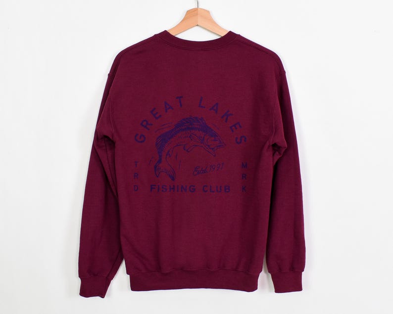 May include: Burgundy long-sleeve sweatshirt with a navy blue graphic of a fish and the text "Great Lakes Trading Co. Fishing Club" on the back.