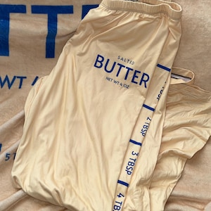 May include: A pair of yellow leggings with a blue "SALTED BUTTER NET WT 4 OZ" logo and a blue stripe down the side with measurements in tablespoons.