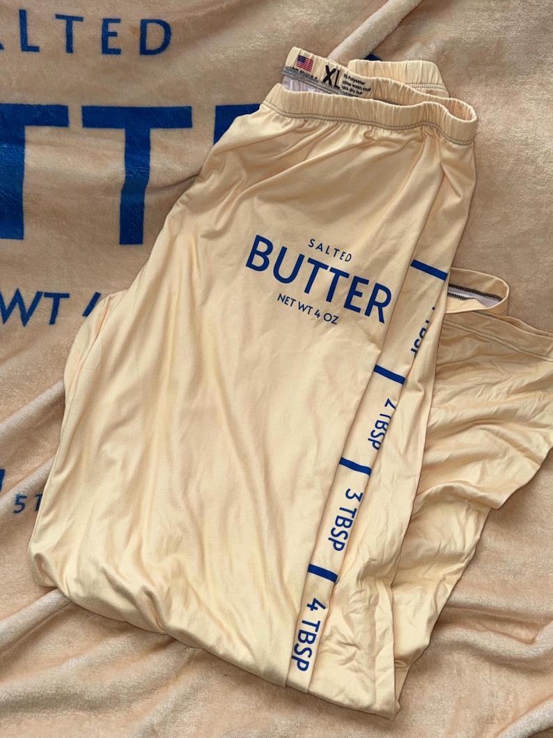May include: A pair of yellow leggings with a blue "SALTED BUTTER NET WT 4 OZ" logo and a blue stripe down the side with measurements in tablespoons.