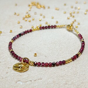 May include: A delicate gold bracelet with a small, textured gold charm. The bracelet is made with tiny red and gold beads.