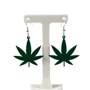May include: A pair of green marijuana leaf dangle earrings on a white display stand.