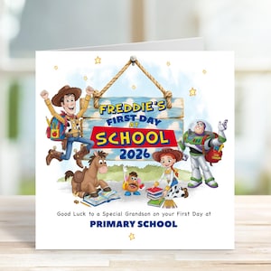 Może przedstawiać: Kwadratowa kartka okolicznościowa z postaciami z Toy Story: Chudym, Buzzem Astralem, Jessie, Cienkim i Panem Bulwą. Nad nimi wisi drewniany szyld z napisem "FREDDIE'S FIRST DAY AT SCHOOL 2026". Poniżej znajduje się tekst "Good Luck to a Special Grandson on your First Day at PRIMARY SCHOOL".