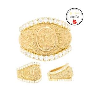 May include: A gold ring with a detailed design and a large center stone surrounded by smaller stones. The ring is set with clear stones and has a wide band.