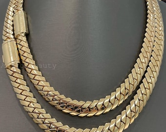 May include: A gold chain necklace with a unique, interlocking design. The chain is made of two strands that are woven together to create a textured look. The necklace is a statement piece that would be perfect for any occasion.