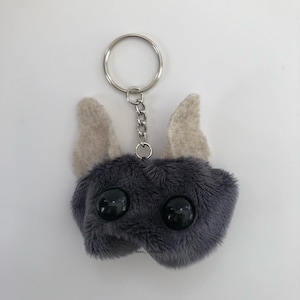 May include: A gray plush keychain with large black eyes and two small beige ears. The keychain is attached to a silver metal ring and chain.