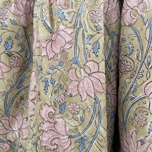 May include: Close-up of fabric with a repeating floral pattern. Large pink flowers with detailed petals are interspersed with smaller flowers and blue leaves on a light green background. The fabric has a soft, textured appearance.