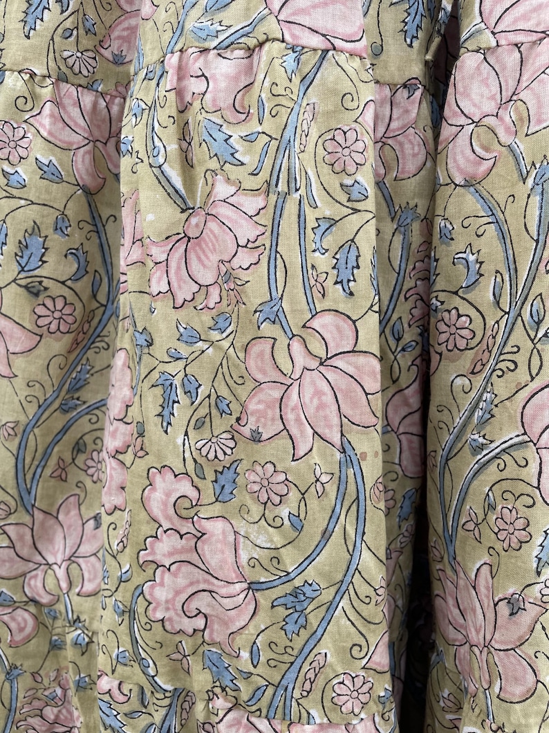 May include: Close-up of fabric with a repeating floral pattern. Large pink flowers with detailed petals are interspersed with smaller flowers and blue leaves on a light green background. The fabric has a soft, textured appearance.