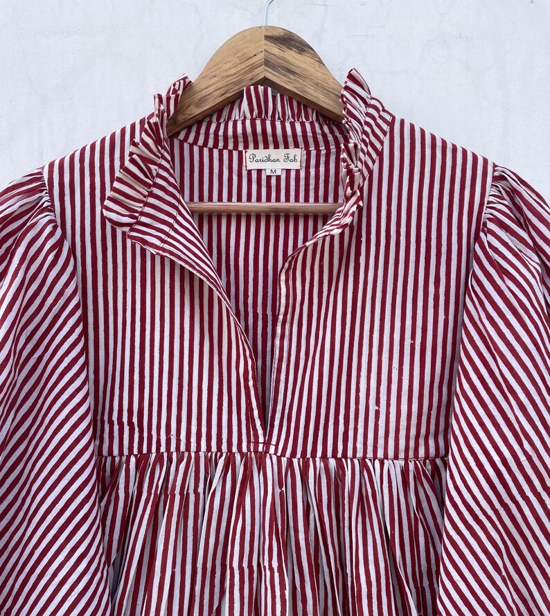 May include: A red and white striped cotton shirt with a ruffled collar and a V-neck. The shirt has a gathered waist and long sleeves. The label reads "Parichhan Fab" and "M".