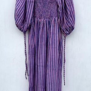 May include: A purple and pink striped midi dress with puffed sleeves and a smocked bodice. The dress has a square neckline and a tiered skirt.