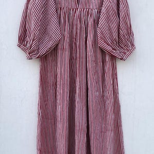 May include: A red and white striped cotton dress with a ruffled neckline and puffed sleeves. The dress has a gathered waist and a loose, flowing fit.