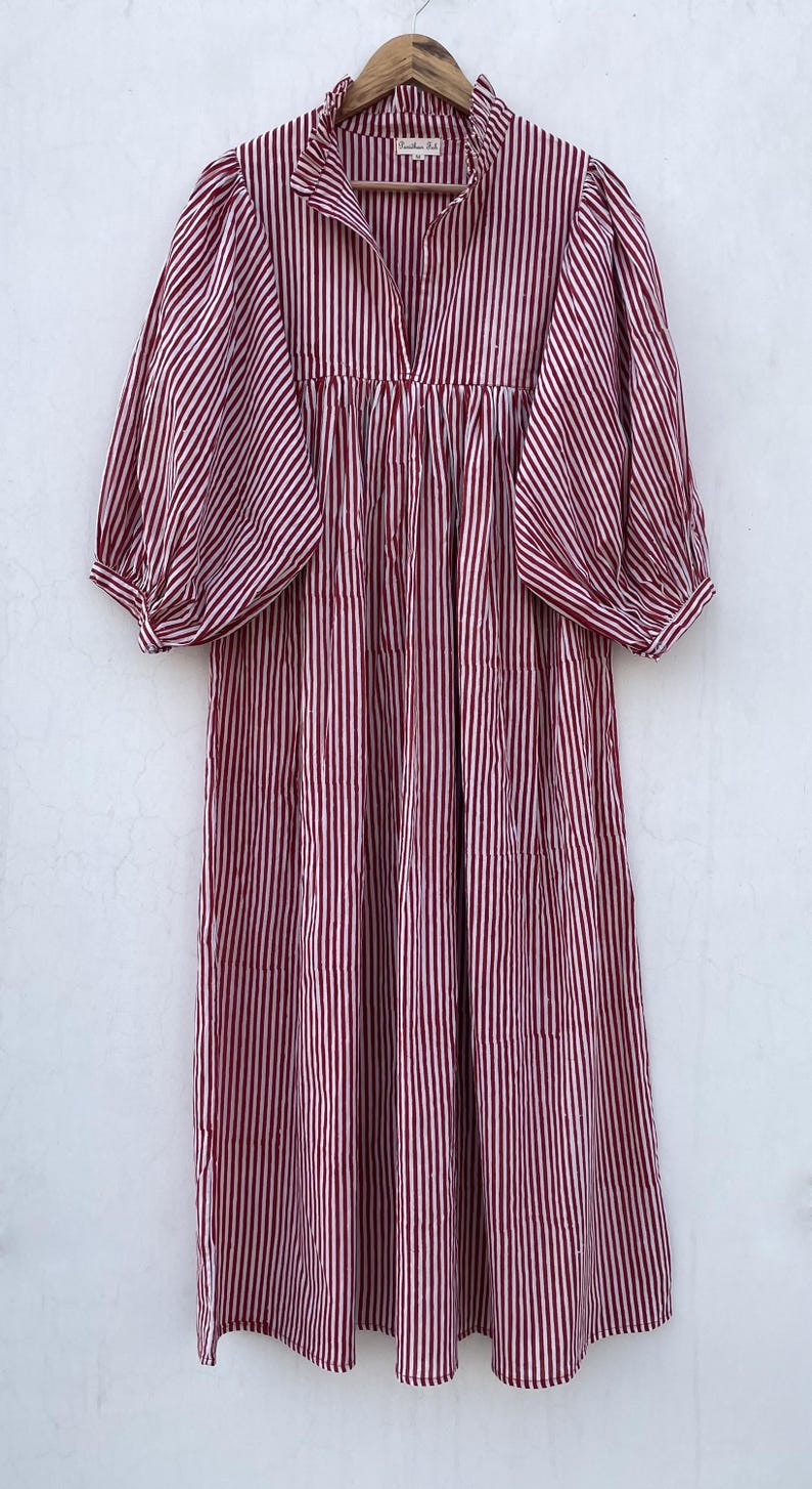 May include: A red and white striped cotton dress with a ruffled neckline and puffed sleeves. The dress has a gathered waist and a loose, flowing fit.