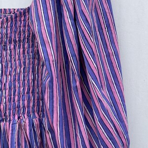 May include: A pink and purple striped dress with a gathered bodice and puff sleeves. The dress is made of a lightweight fabric and has a relaxed fit.