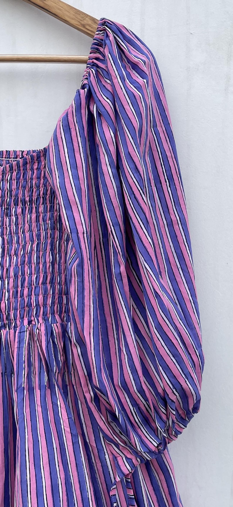 May include: A pink and purple striped dress with a gathered bodice and puff sleeves. The dress is made of a lightweight fabric and has a relaxed fit.