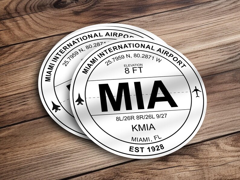 May include: White round sticker with black text that reads "Miami International Airport" and "MIA". The sticker also includes the airport code "KMIA", the city "Miami, FL", and the year "EST 1928".