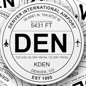 May include: Close-up of a white airport sticker with black text. The sticker reads "DENVER INTERNATIONAL AIRPORT", "DEN", "KDEN", "DENVER, CO", "EST 1995", and "ELEVATION 5431 FT".