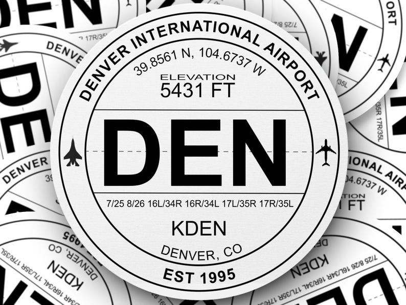 May include: Close-up of a white airport sticker with black text. The sticker reads "DENVER INTERNATIONAL AIRPORT", "DEN", "KDEN", "DENVER, CO", "EST 1995", and "ELEVATION 5431 FT".