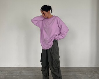 May include: A person wearing a light purple long-sleeve shirt and dark green cargo pants. The person is also wearing white and pink sneakers. The outfit is casual and comfortable, suitable for everyday wear.