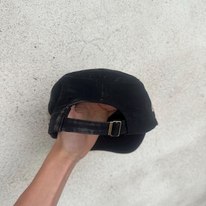 May include: Black cap with a curved brim and adjustable strap. The strap features a brass-colored buckle. The cap is made of a dark fabric and appears to be slightly worn. The cap is a classic style.