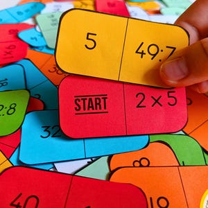 Può includere: Primo piano di un gioco colorato con tessere a forma di domino che presentano problemi di matematica e numeri. Le tessere sono rosse, gialle, blu, verdi e arancioni. Una tessera dice "START" e un'altra "49:7".