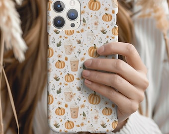 May include: A smartphone case featuring a repeating pattern of orange pumpkins, beige coffee cups with whipped cream, and small brown leaves on a white background. The case has a cutout for a triple-lens camera system on the upper left side.