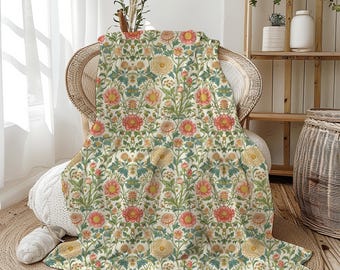 May include: A floral patterned blanket draped over a wicker chair. The blanket features a repeating design of pink, yellow, and blue flowers with green leaves on a cream background. The blanket is made of a soft material.