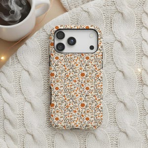 May include: A smartphone case featuring a repeating pattern of orange and brown flowers with thin dark brown stems and leaves on a cream background. The case has a rectangular camera cutout with three circular lenses and a small circular flash.