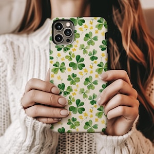 May include: A white phone case with a green shamrock pattern and yellow flower accents. The case is designed for an iPhone.