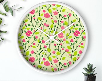 May include: A white round clock with a floral design. The clock face features a pattern of pink flowers and green leaves on a light yellow background.