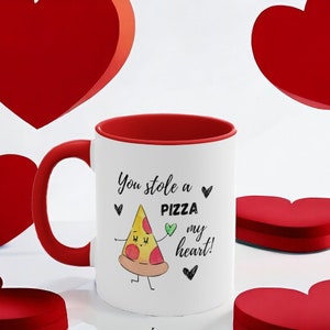 May include: White ceramic mug with a red interior and handle. The mug features the text "You stole a pizza my heart!" along with a cartoon pizza slice illustration and small heart graphics. The mug is a Valentine's Day themed gift.