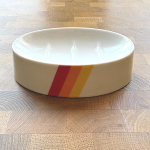 Puede incluir: Una taza de cerámica blanca con un asa negra y el texto "But First, Coffee" en negro y negrita. La taza está sobre una superficie blanca.