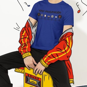 May include: A person wearing a blue t-shirt with the text "Vinyl Destination" and a graphic of vinyl records, cassette tapes, and a CD. The person is wearing headphones and a red jacket with yellow stripes. A yellow speaker with the word "SOUND" is in the image.