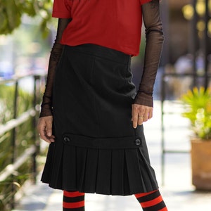 May include: A person wearing a red t-shirt with the text "Vinyl Destination" and vinyl record graphics. The person is also wearing a black skirt, striped red and black leggings, and black platform boots.