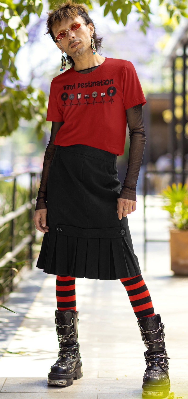 May include: A person wearing a red t-shirt with the text "Vinyl Destination" and vinyl record graphics. The person is also wearing a black skirt, striped red and black leggings, and black platform boots.