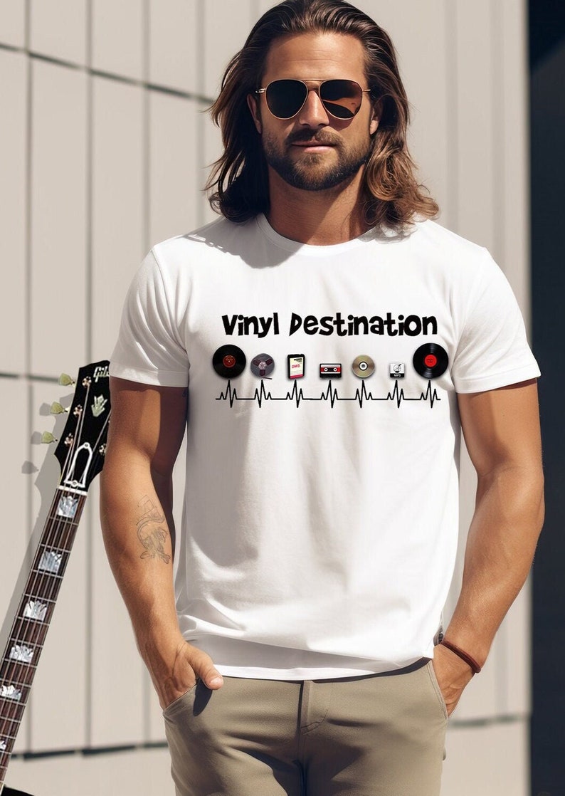 May include: White t-shirt with the text "Vinyl Destination" above a series of music-related icons, including vinyl records, a smartphone, and a CD. The design is set against a heartbeat line. A guitar is leaning against a wall.