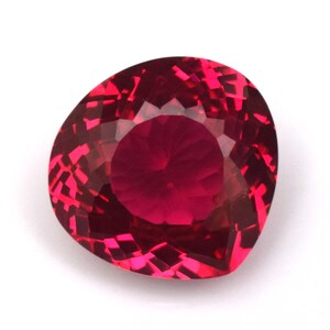 May include: A faceted, heart-shaped gemstone with a deep red hue. The gem's surface reflects light, showcasing its intricate cuts and internal structure. The stone is set against a white background, highlighting its color and clarity. This gemstone is suitable for jewelry.