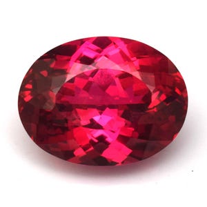Puede incluir: Una gema facetada, de forma ovalada, en un tono rojo vibrante. La superficie de la gema refleja la luz, mostrando sus intrincados cortes y estructura interna. La gema se encuentra sobre un fondo blanco.
