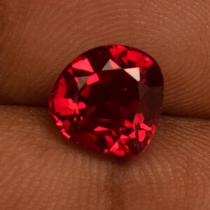 May include: A deep red gemstone with a faceted cut. The gemstone is a heart shape and has a high polish.